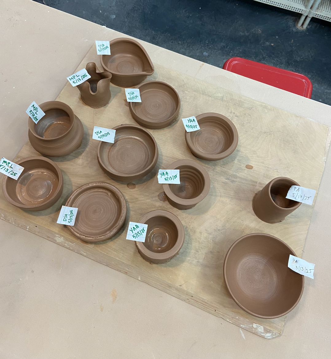 Collection of small ceramic pots on a wooden board with name tags.